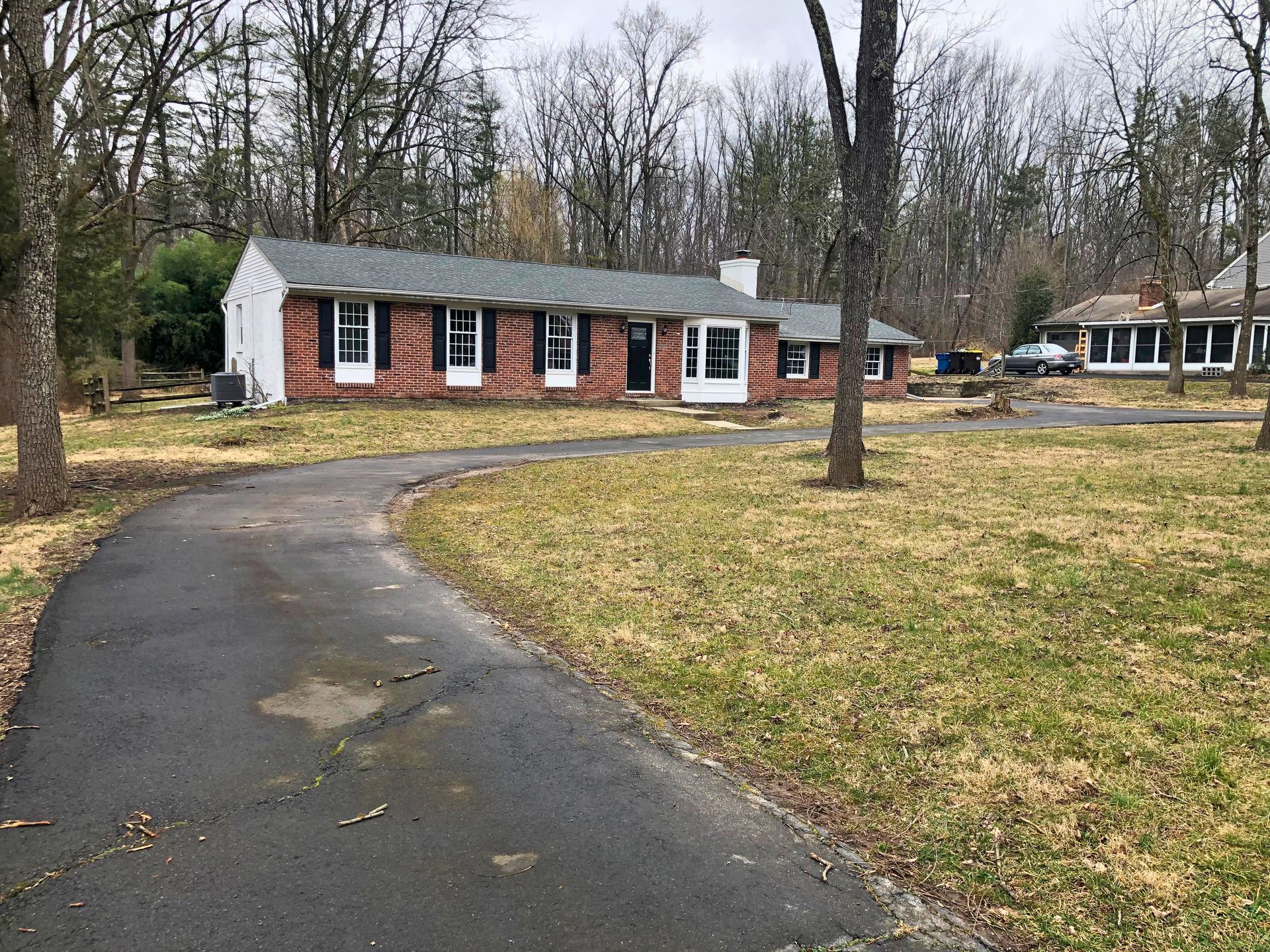 Brick ranch house with black shutters, long driveway, and bare trees.