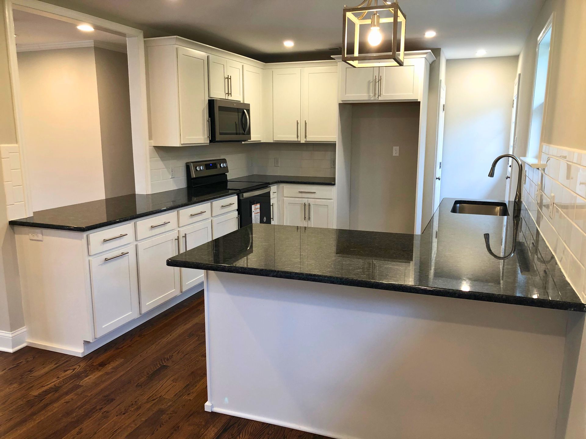 A modern white kitchen with black countertops, stainless steel appliances, and a large island with seating.