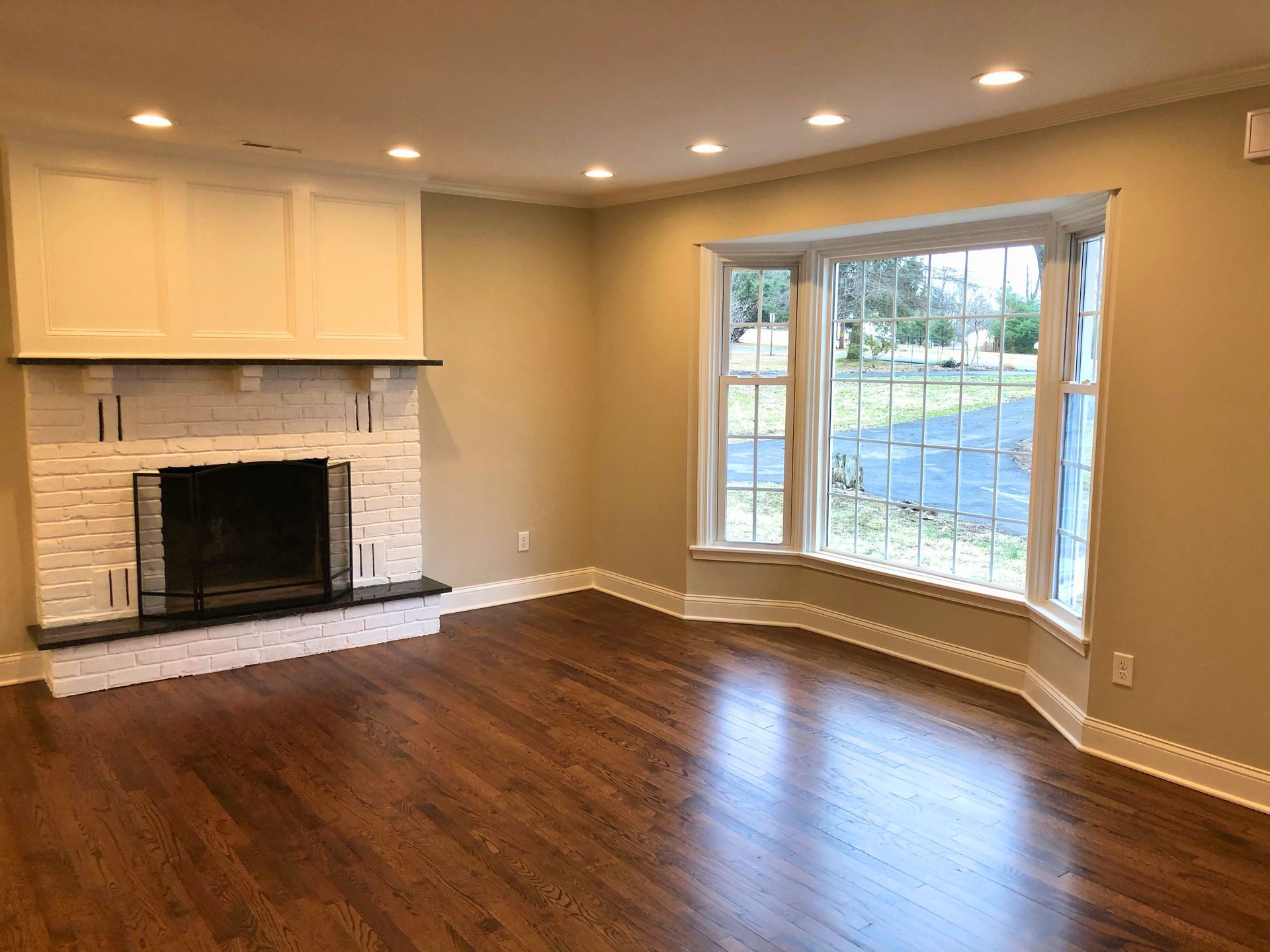 Living room with a fireplace, bay window, and hardwood floors.