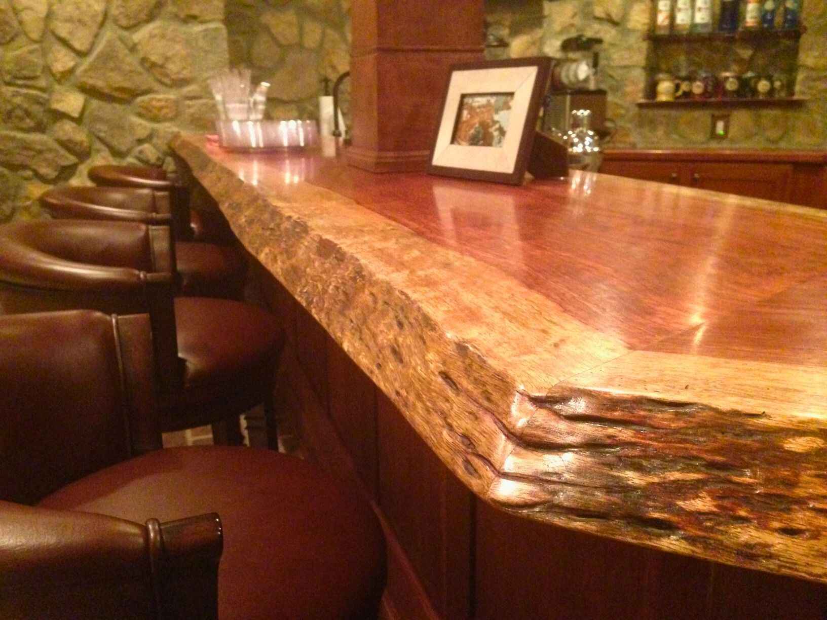 Wooden bar with live edge, brown leather chairs, and a stone wall background.