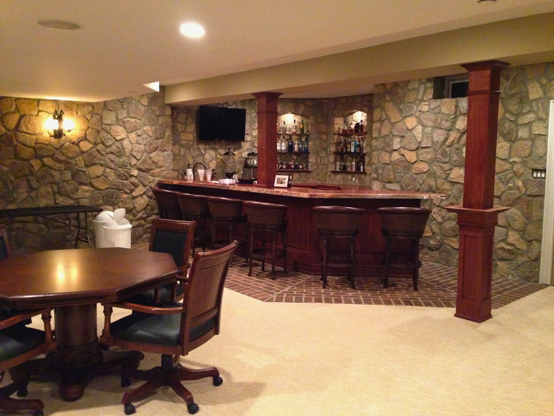 Basement bar with stone wall, mahogany bar, bar stools, and a table with chairs.