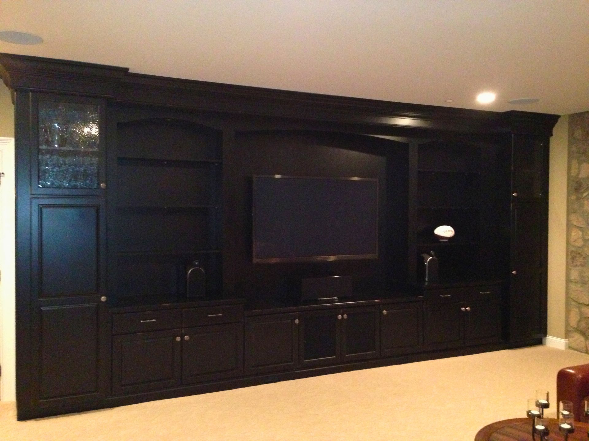 Dark wood entertainment center with TV, shelves, and cabinets against a beige wall.