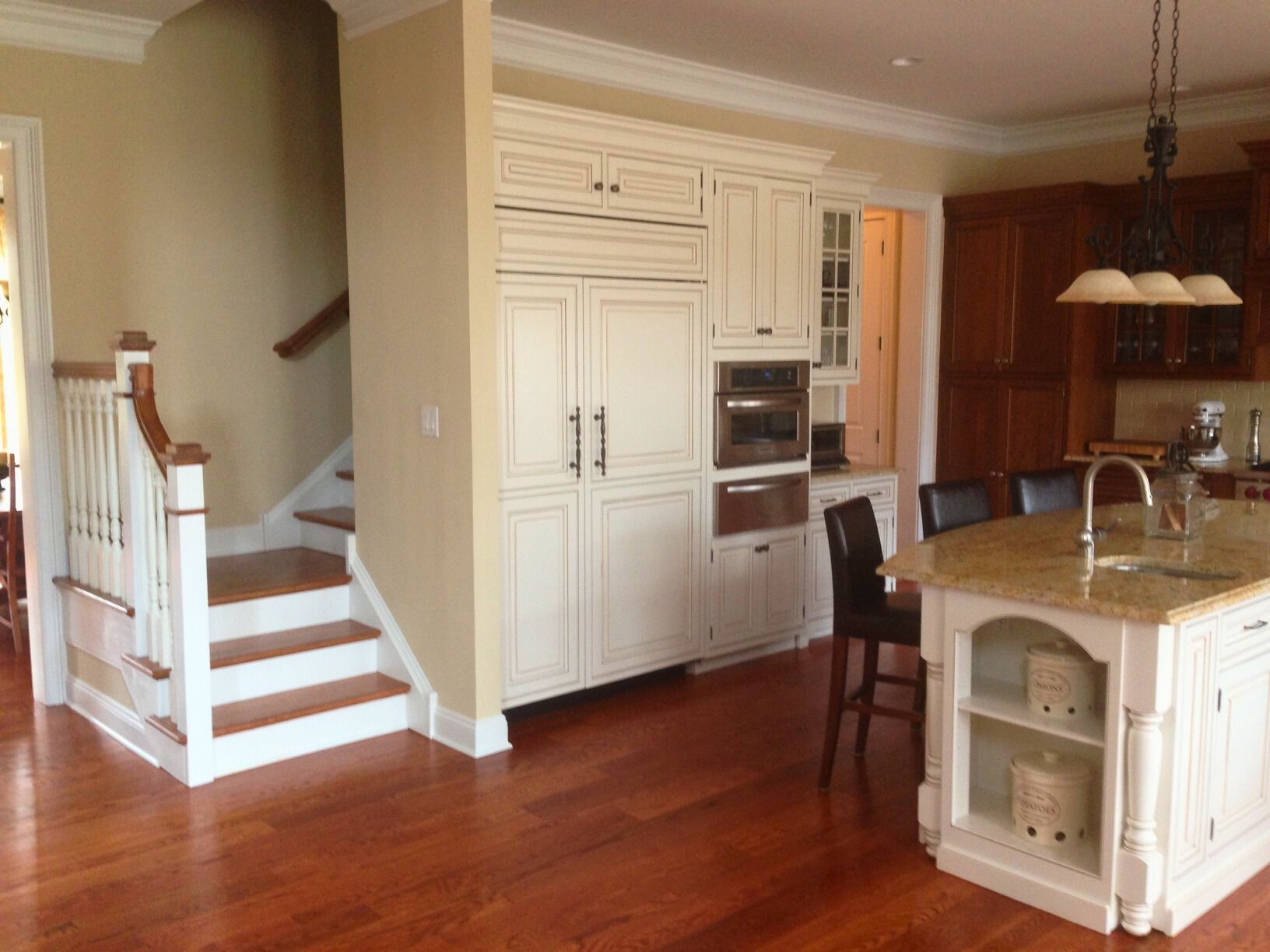 Kitchen with island and built-in fridge near stairs. Wood floors, beige walls, cream cabinets.