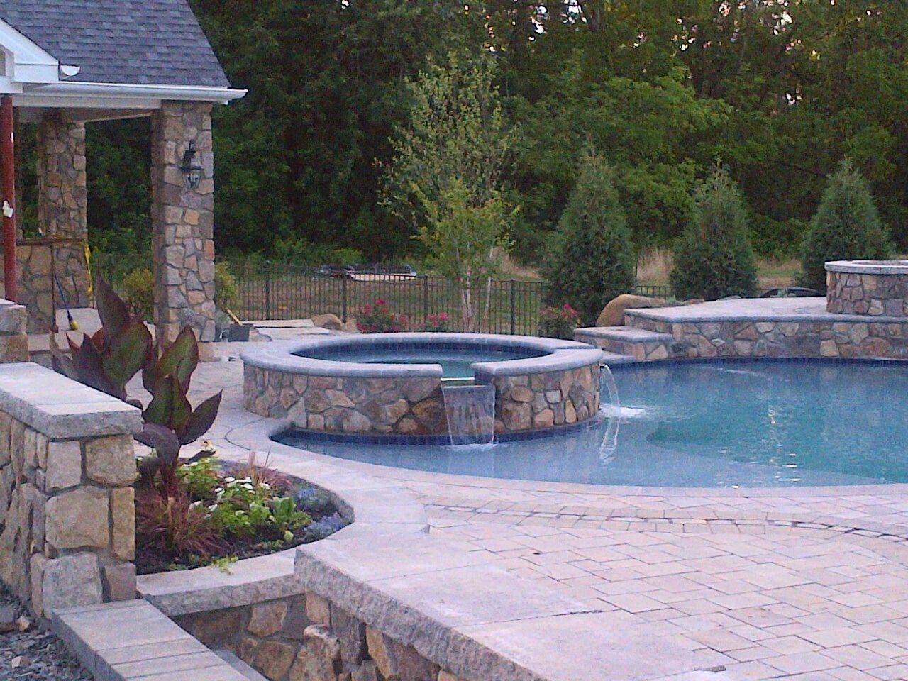 Stone-lined pool with waterfall feature, surrounded by patio and landscaping.