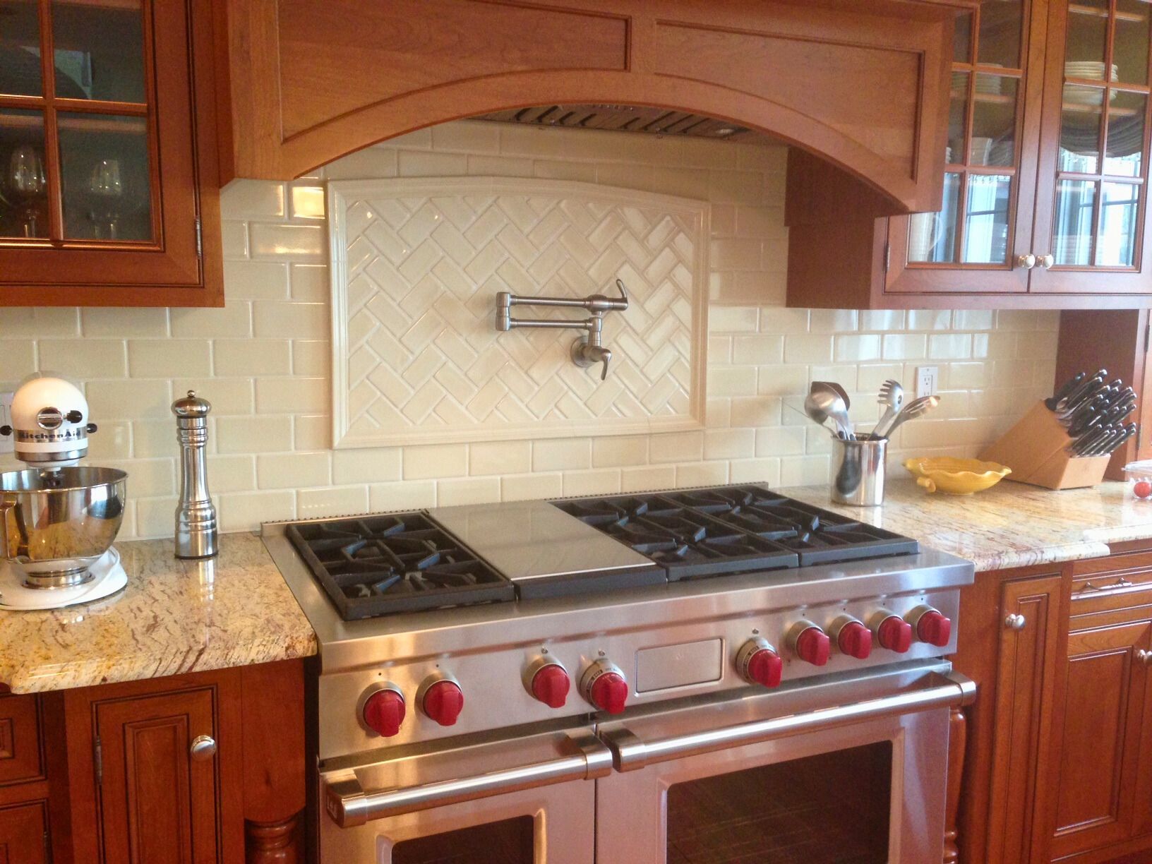 Kitchen with stainless steel range, red knobs, wooden cabinets, beige tiled backsplash, and a mixer.