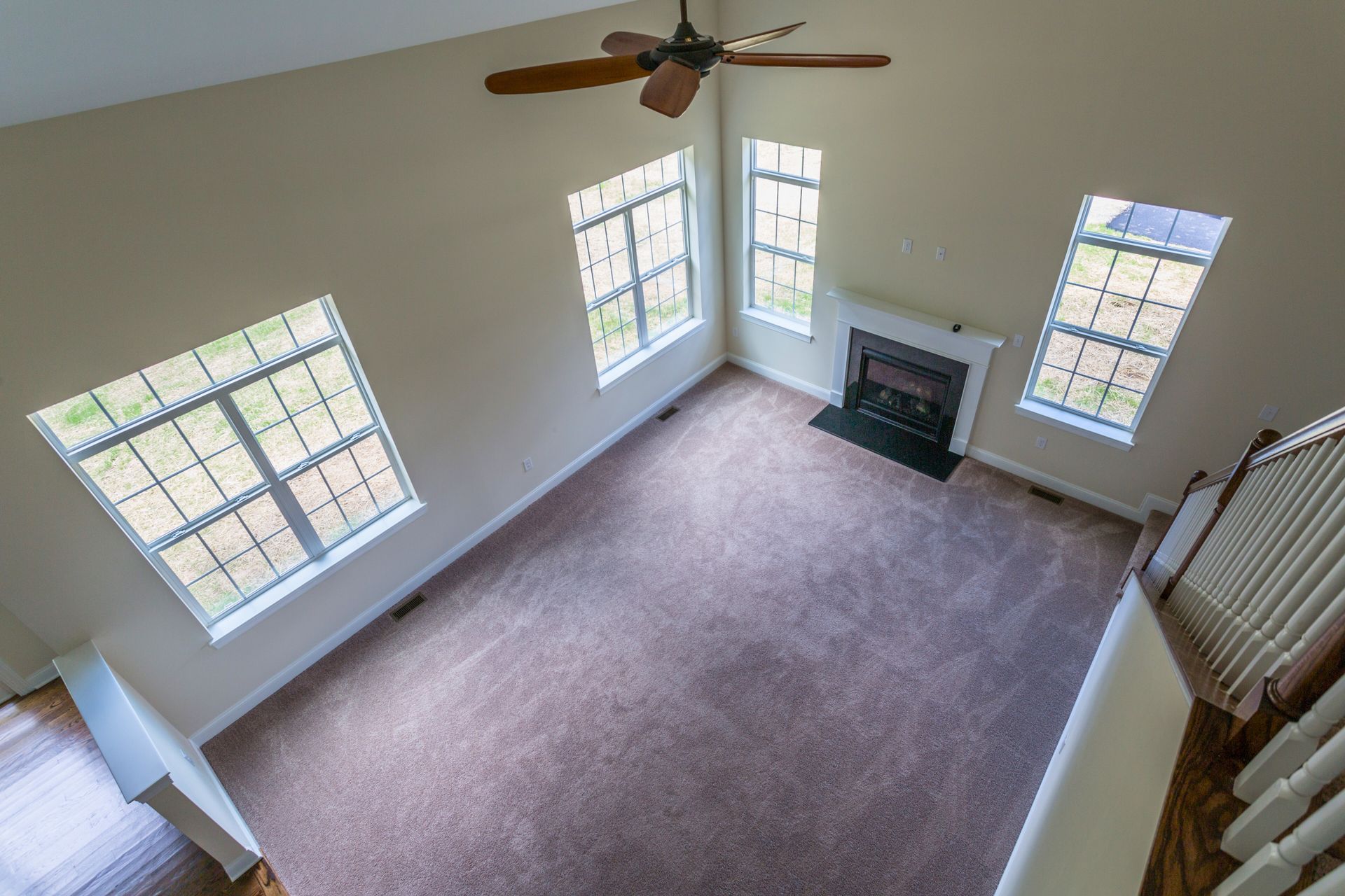 High-angle view of a spacious room with carpet, windows, fireplace, and a ceiling fan.