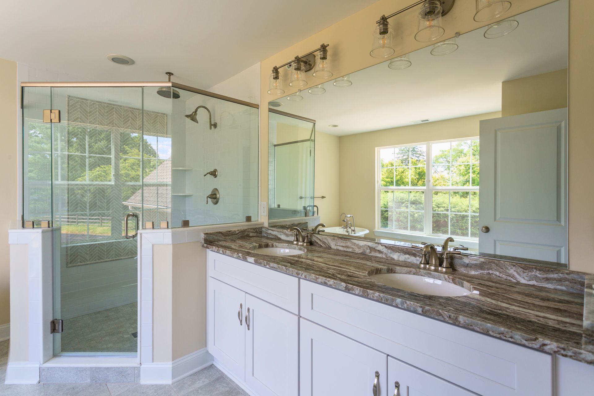 Spacious bathroom with glass shower, double vanity with marble countertop, and large window.