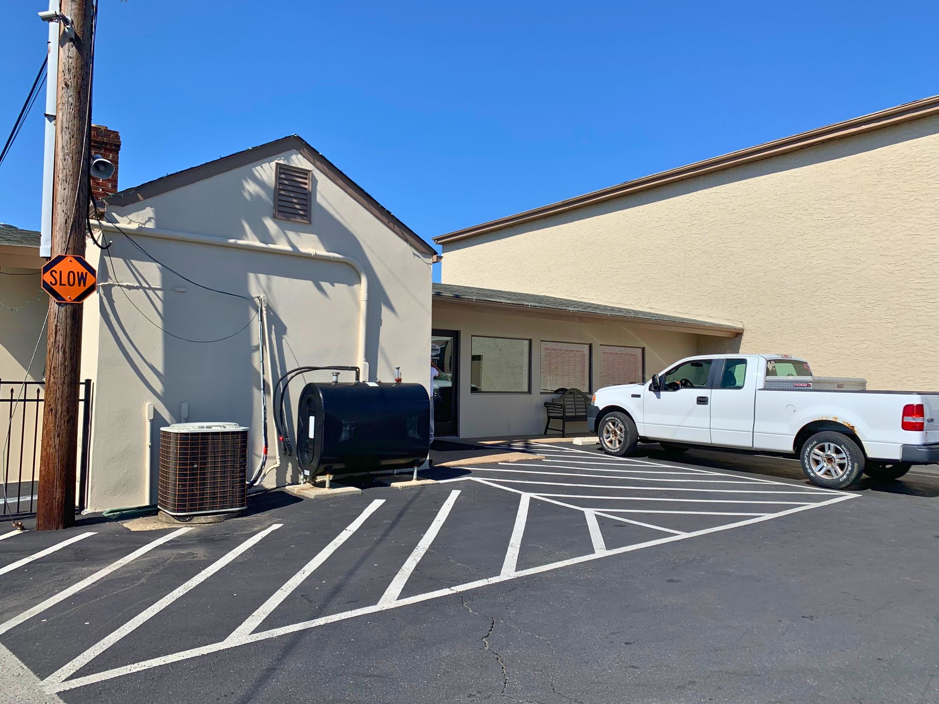 A white pickup truck parked in front of a light-colored building with a blue sky.