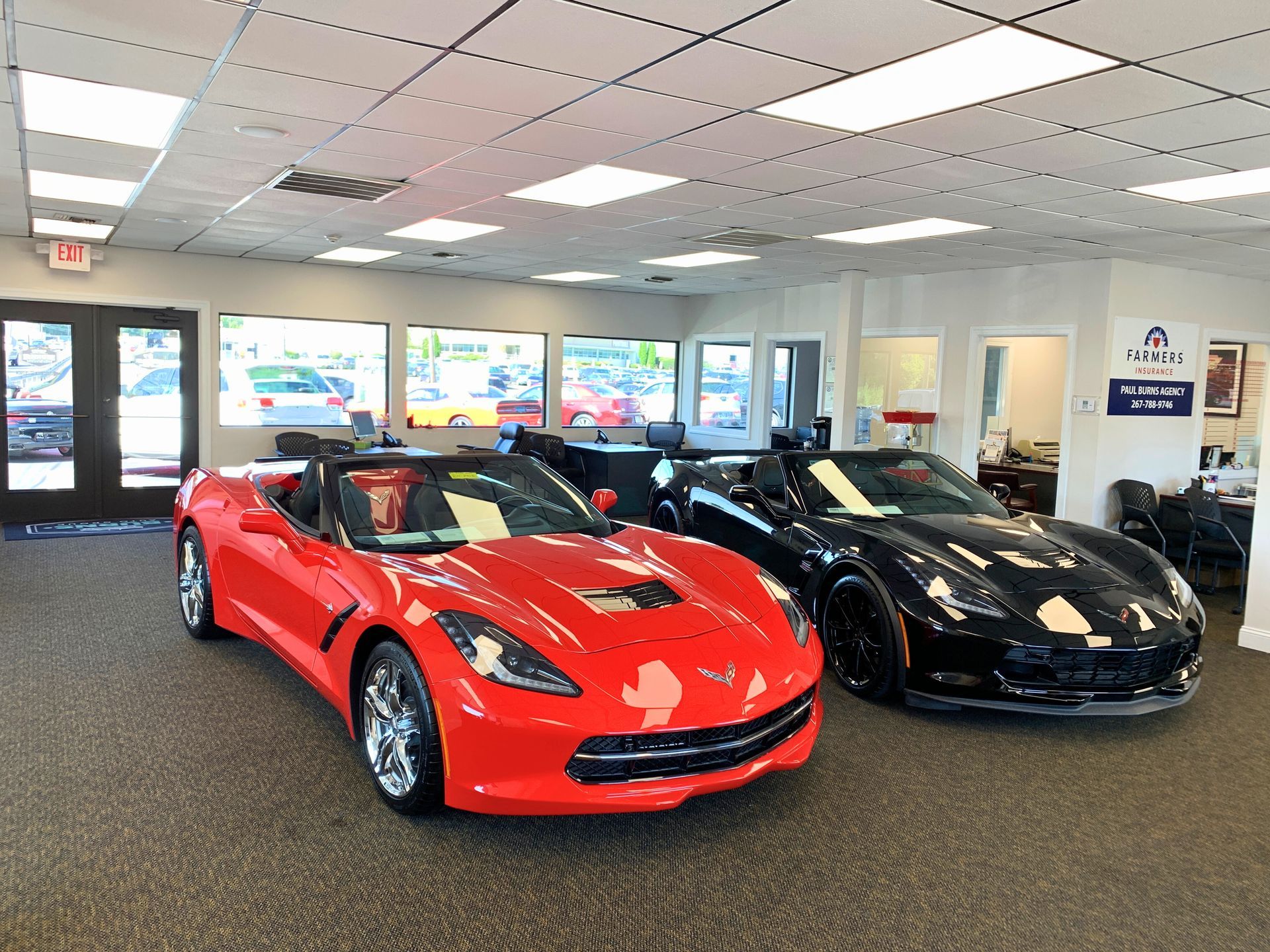 Red and black convertible Corvettes on display inside a car dealership showroom.