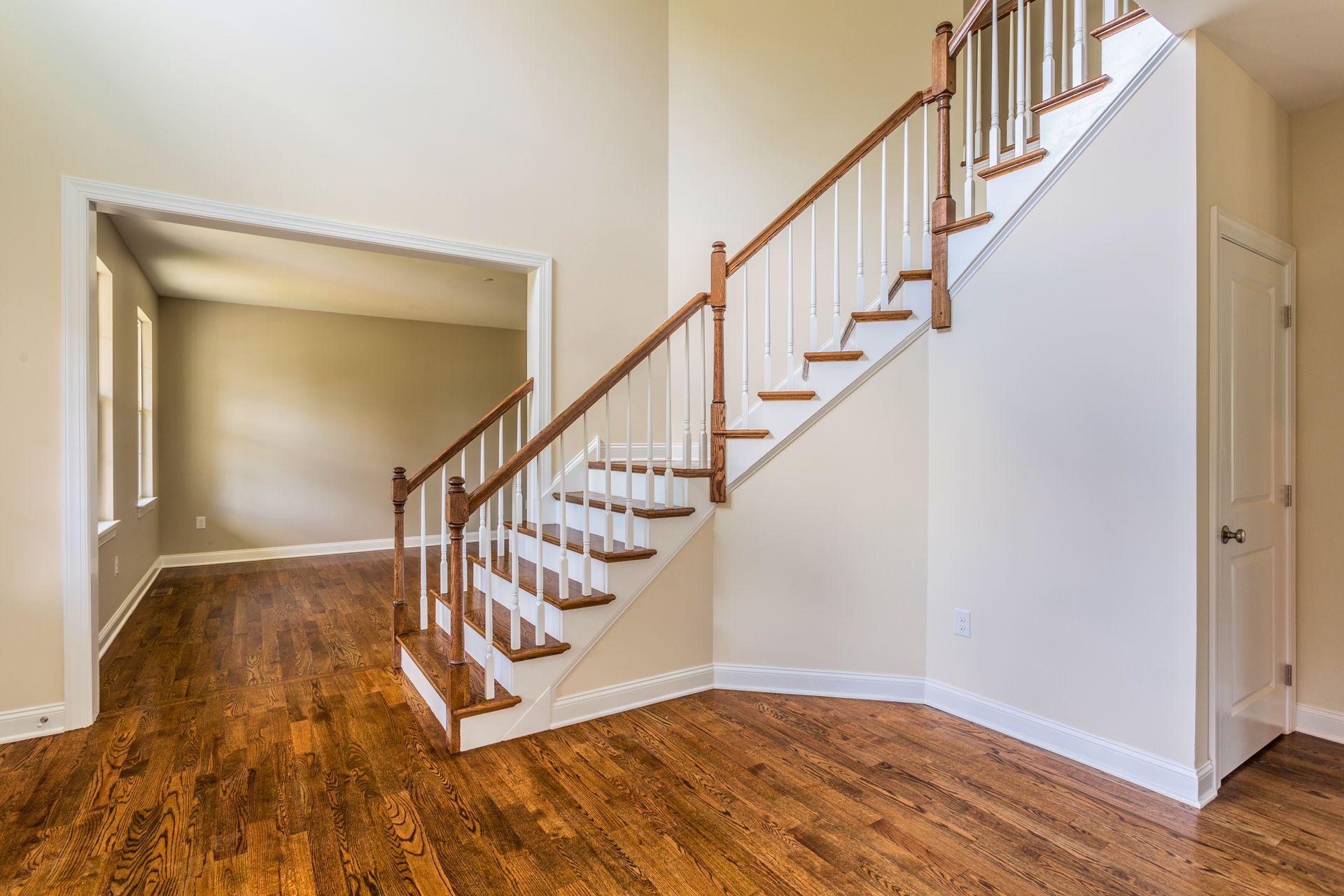 Interior of a house with a staircase, hardwood floors, and an adjacent room with windows.