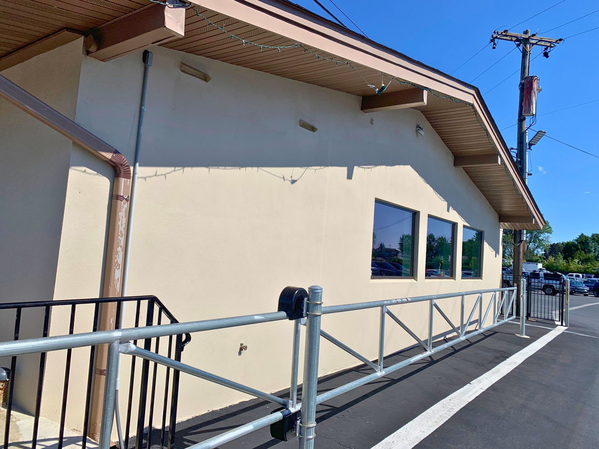 Exterior view of a beige building with a ramp and railing, blue windows, and a brown roof.