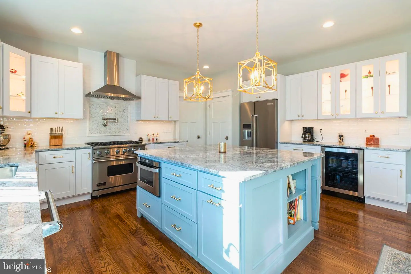 Spacious kitchen with blue island, white cabinets, wood floors, granite countertops, and gold light fixtures.