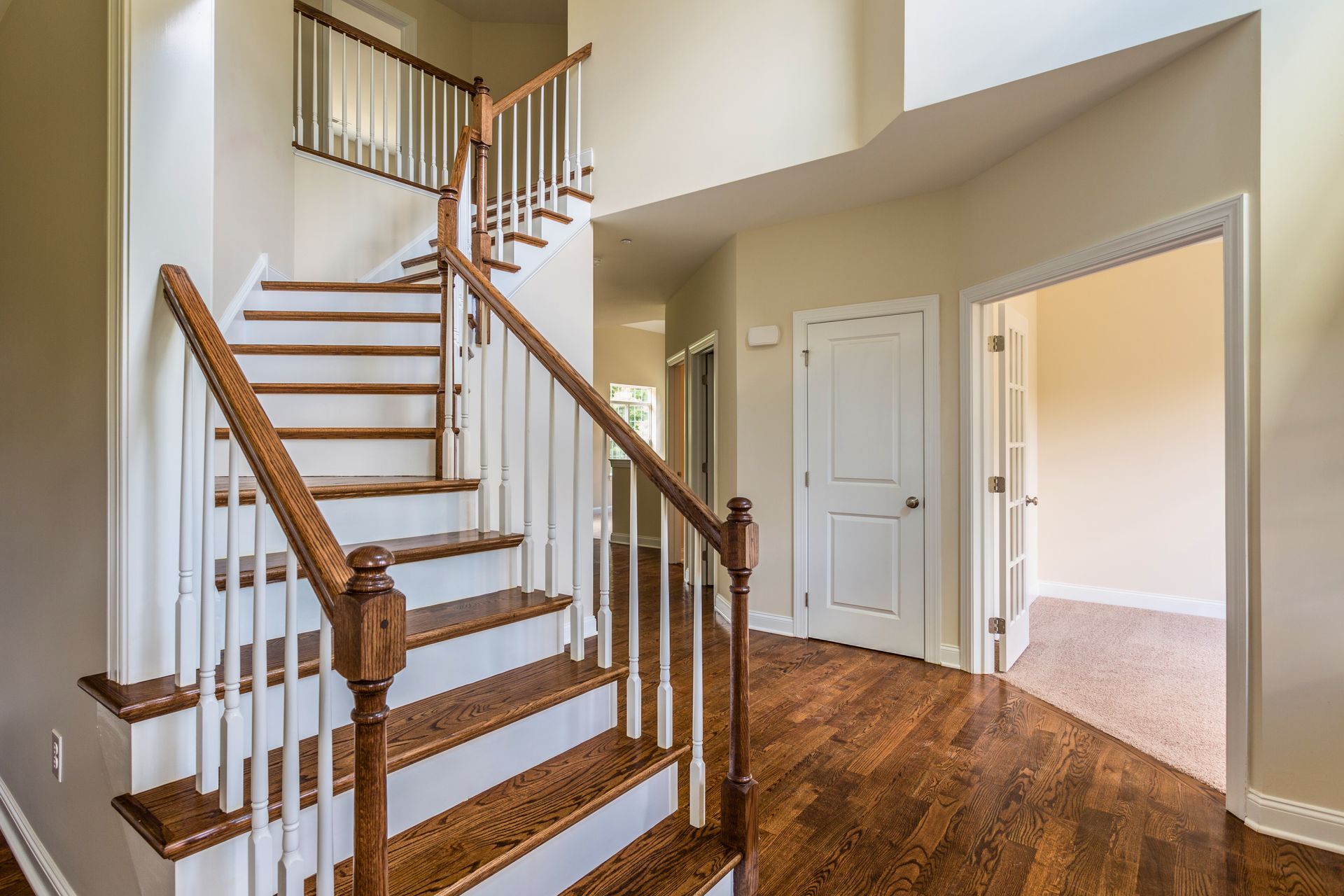 Wooden staircase in a home's entryway, leading to a second floor. Dark hardwood floor, white walls, and door to a room.