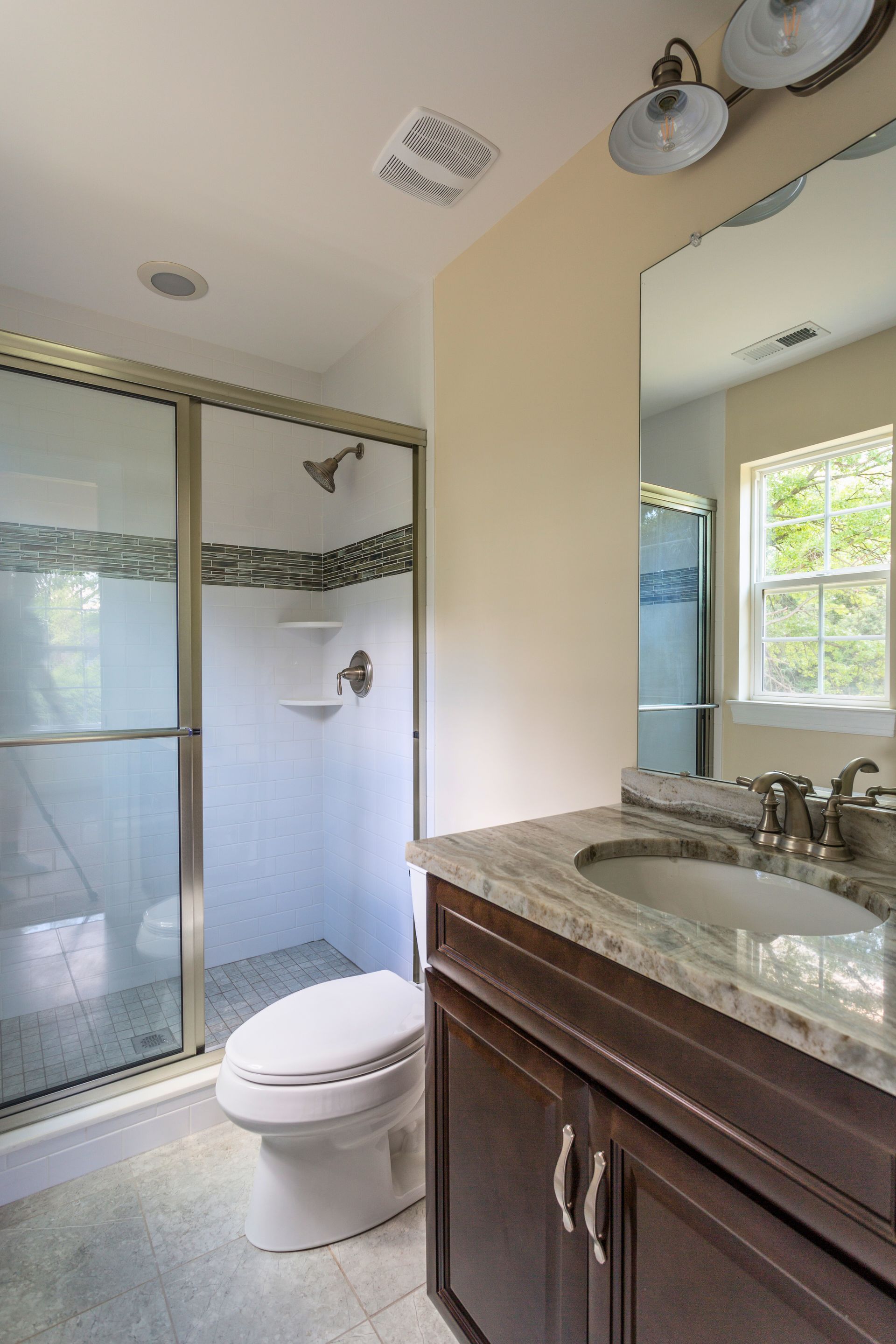 Bathroom with shower, toilet, vanity, and window; light beige walls, dark wood vanity, and white fixtures.