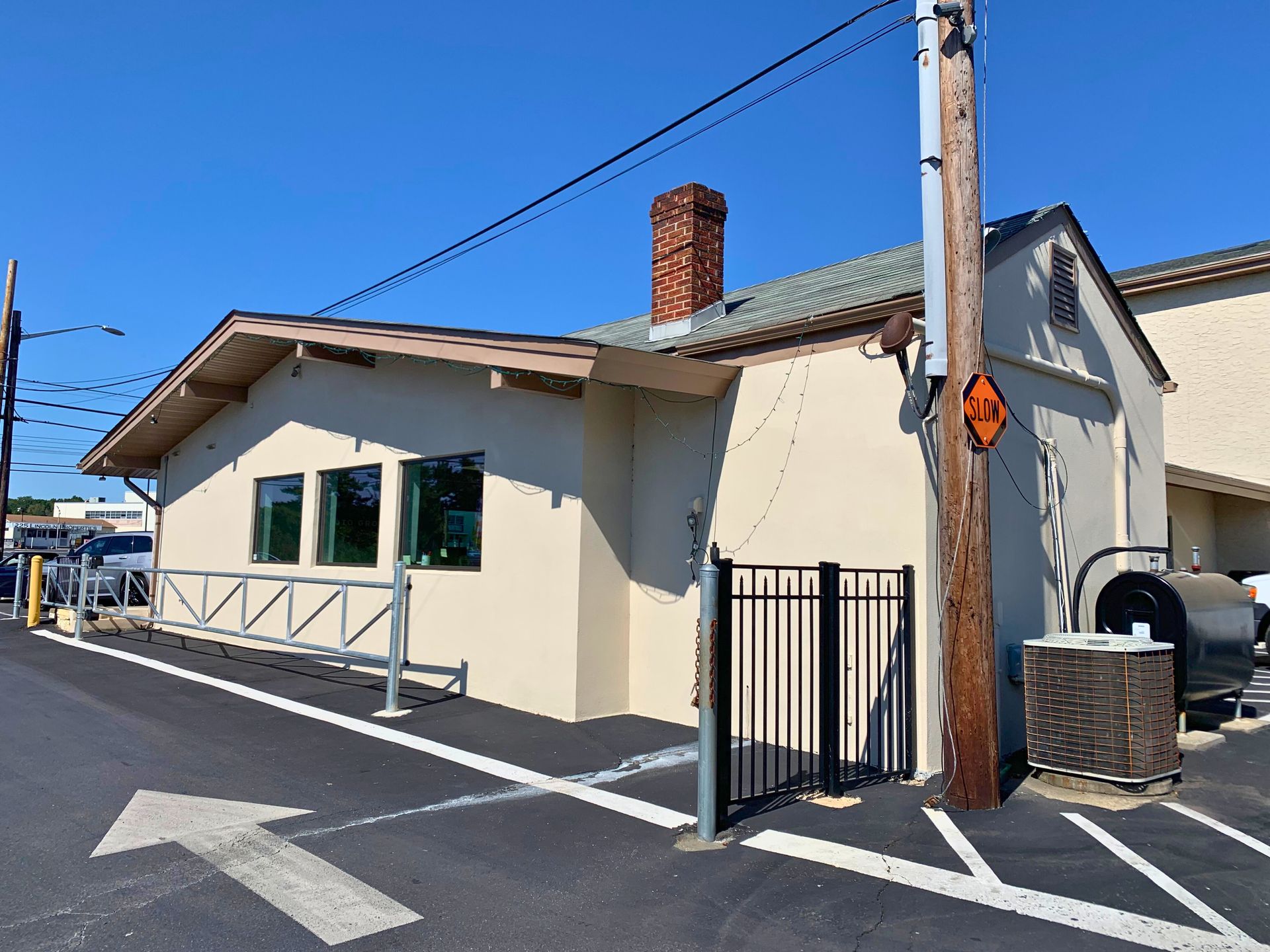 Tan building with a black gate, chimney, and an air conditioning unit; parking lot with an arrow.