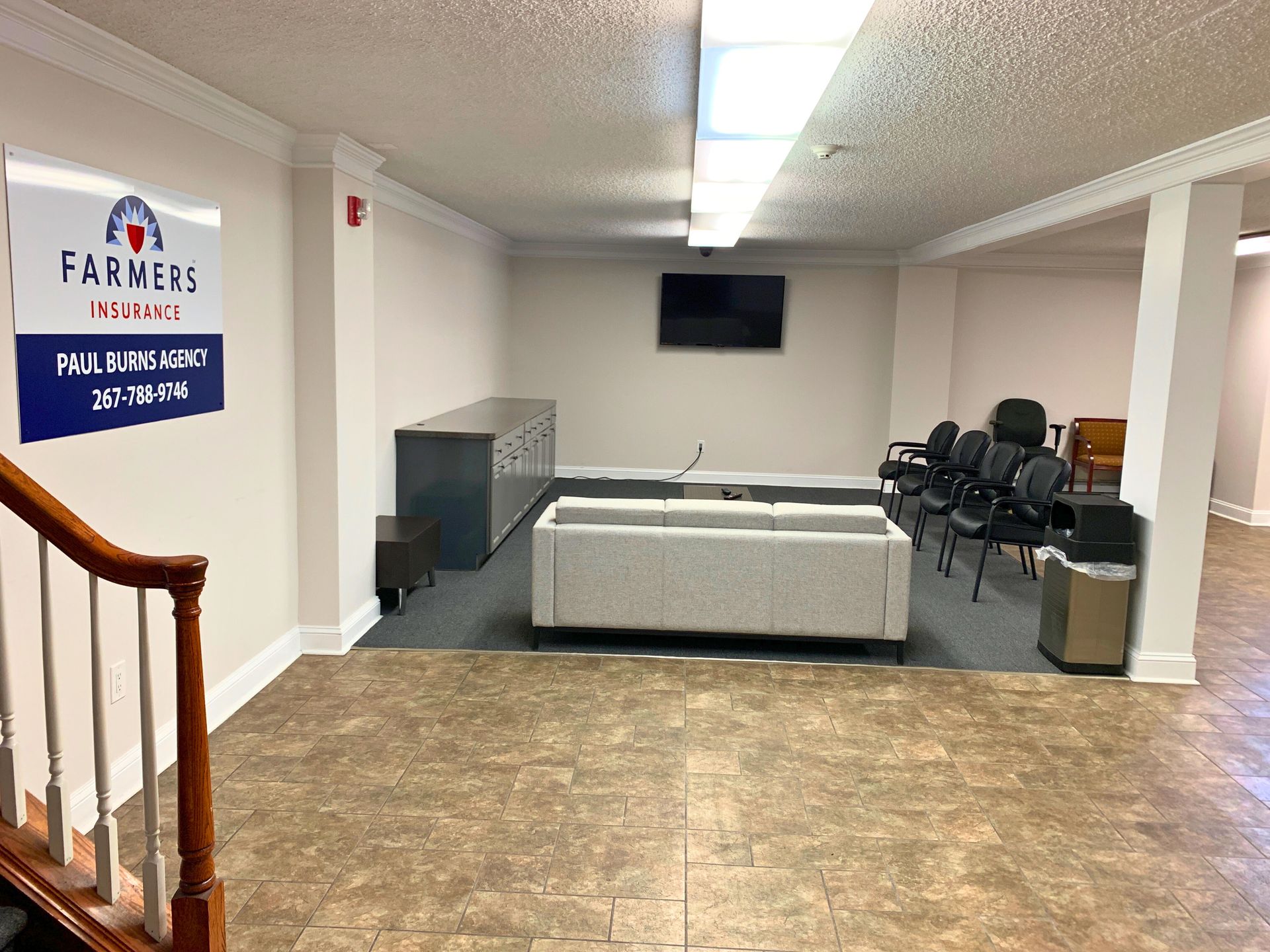 Waiting area in an office with seating, a TV, and Farmers Insurance sign.