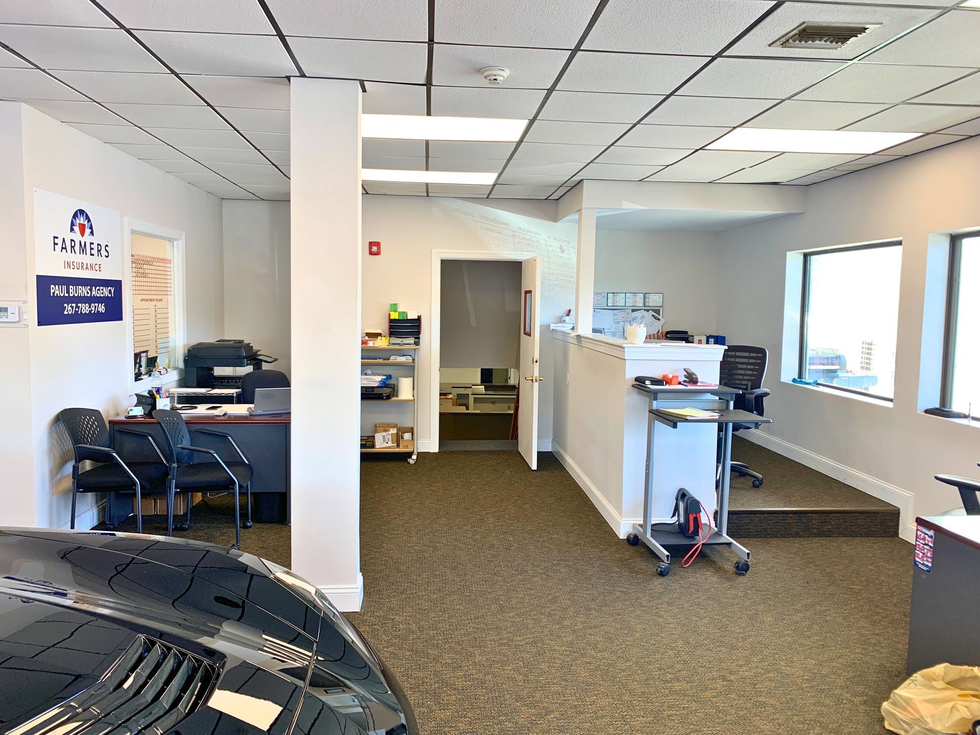 Interior of a car dealership office with desks, a reception area, and a doorway.