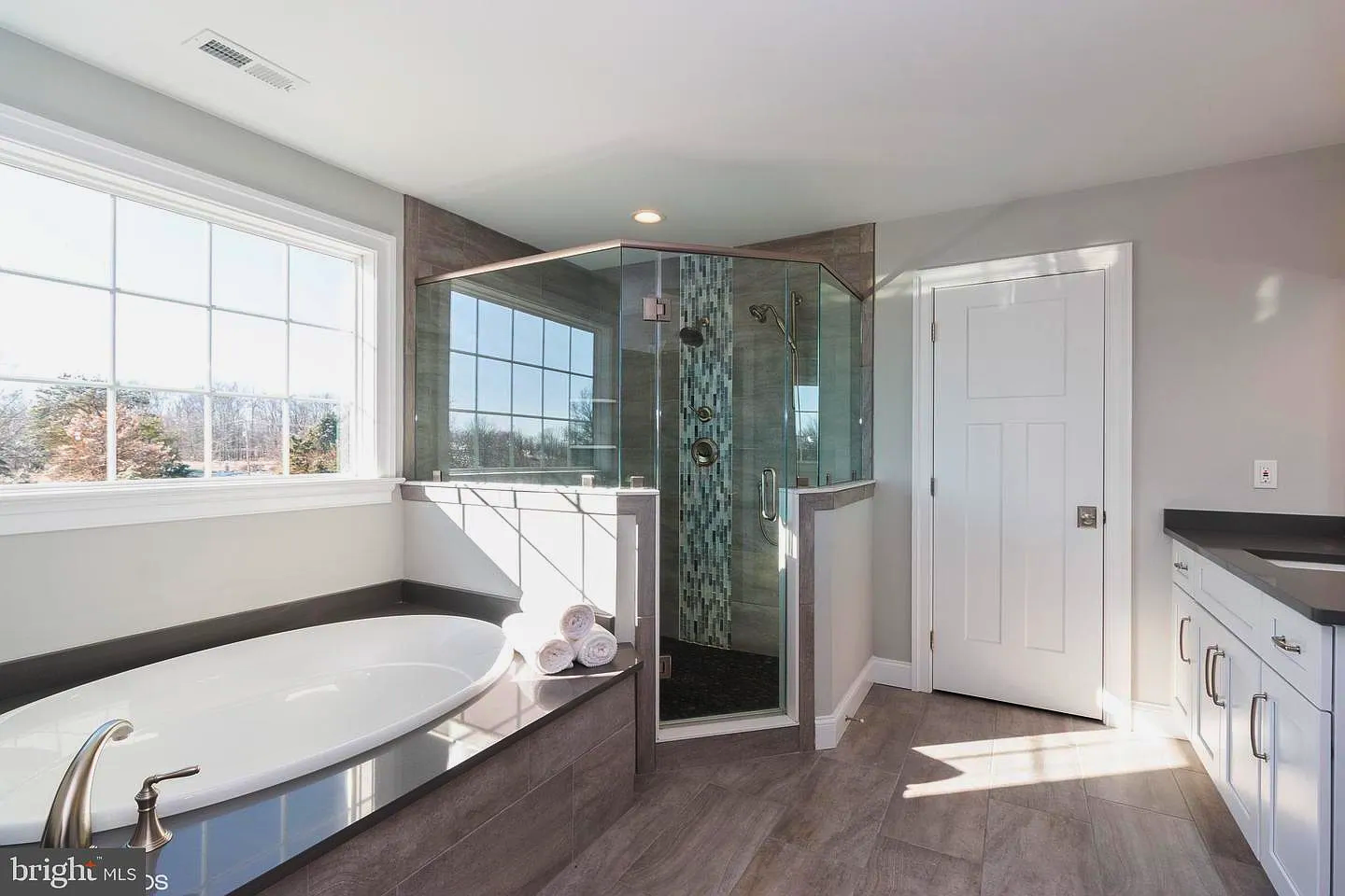 Spacious modern bathroom with a tub, glass shower, and white cabinets.