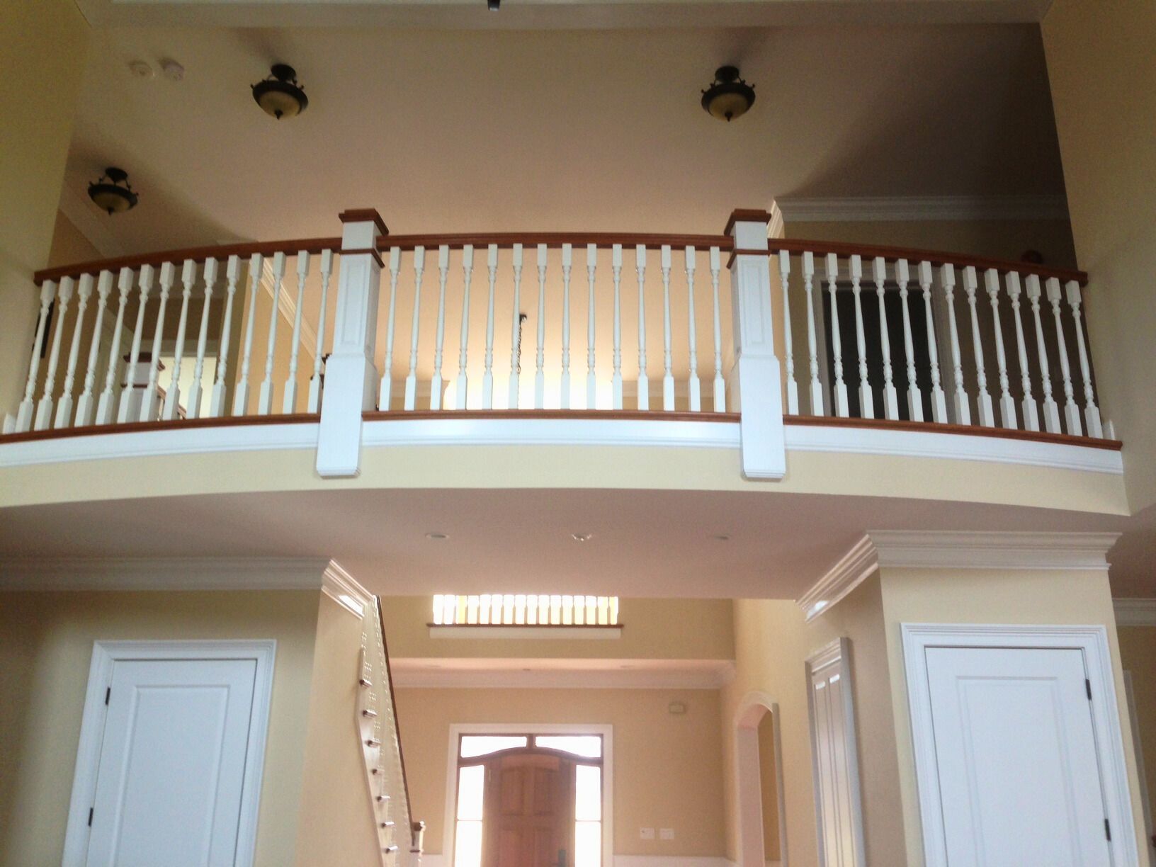 Interior view of a two-story foyer with a balcony, white railing, and yellow walls.
