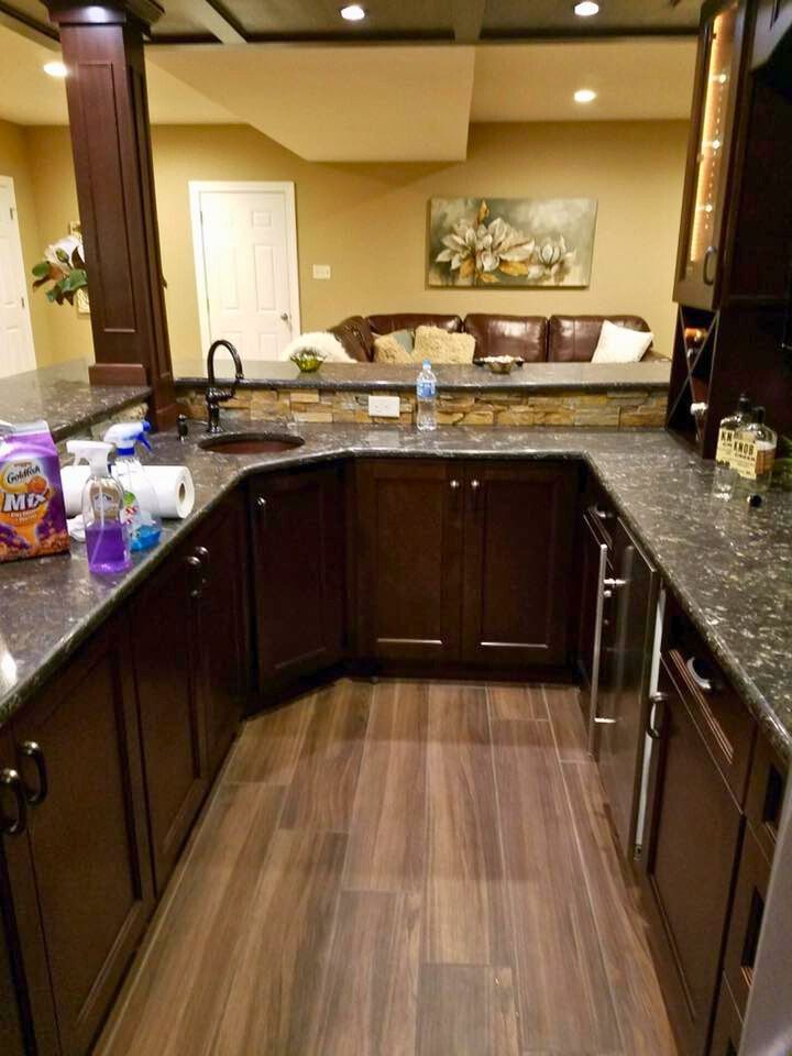 A basement kitchen with dark brown cabinets, granite countertops, and a stainless steel refrigerator.