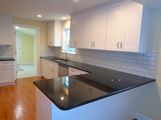 Kitchen with white cabinets, black countertop, subway tile backsplash, and hardwood floor.