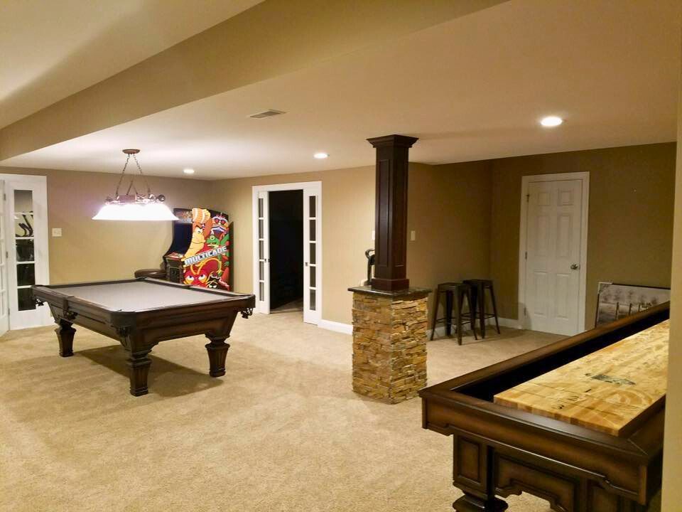 Finished basement with pool table, arcade game, shuffleboard, bar stools, and neutral color scheme.
