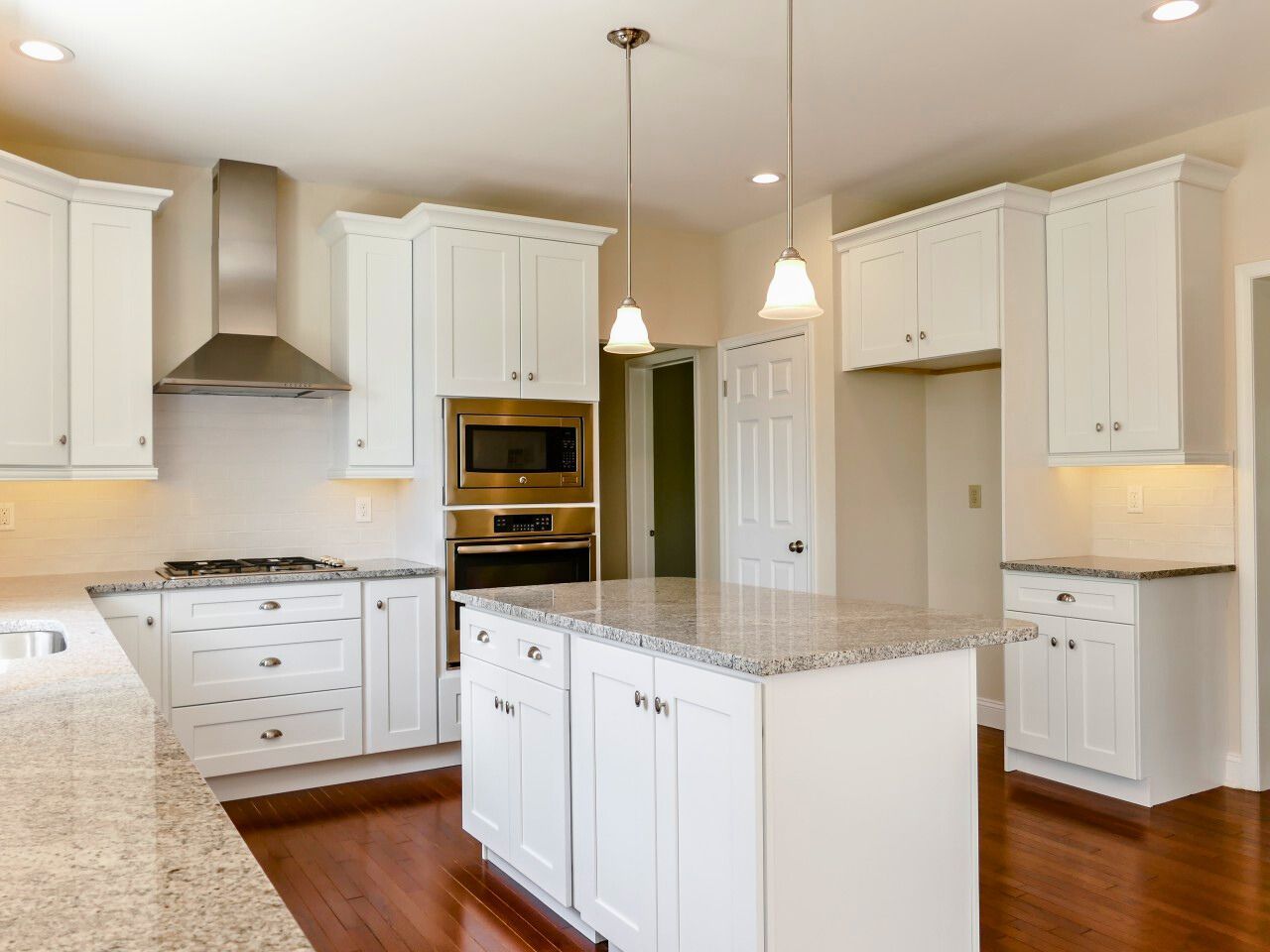 White kitchen with island, granite countertops, stainless steel appliances, and hardwood floors.