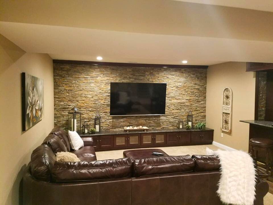 A brown leather sectional couch faces a wall with a large TV and stone accent.
