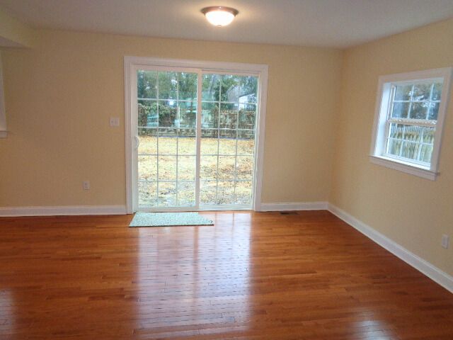 Empty room with sliding glass door and window, hardwood floors, and light yellow walls.