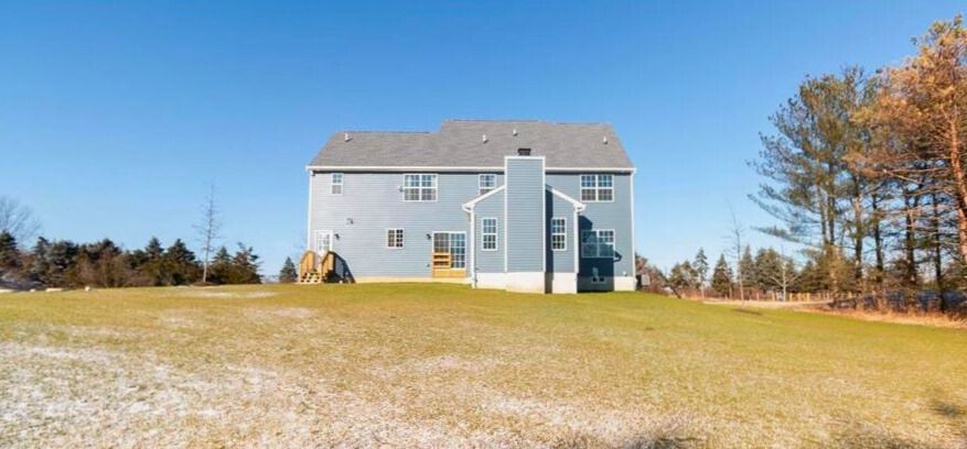 A two-story blue house on a grassy hill with a clear blue sky in the background.