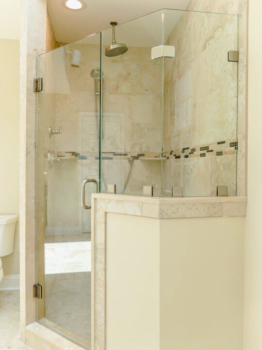 Corner shower with glass doors, marble accents, and a beige tile interior.