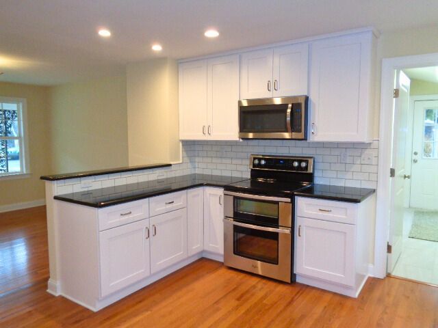 White kitchen cabinets with black countertops, stainless steel appliances, and light wood floors.