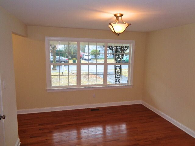 Empty room with hardwood floor, window, tan walls, and a ceiling light.