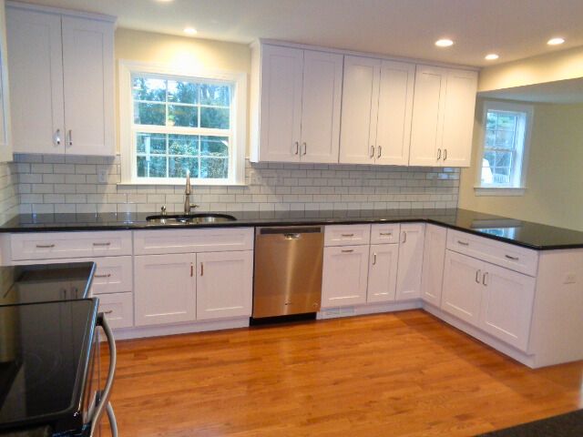 White kitchen cabinets, black countertops, stainless steel dishwasher, wood floor.