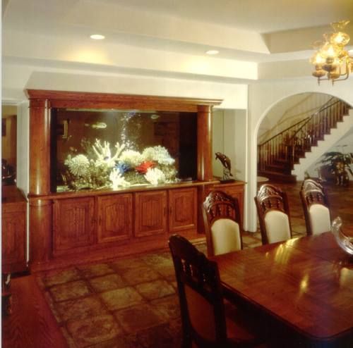 Large aquarium built into wood cabinetry in a dining room with stairs in the background.