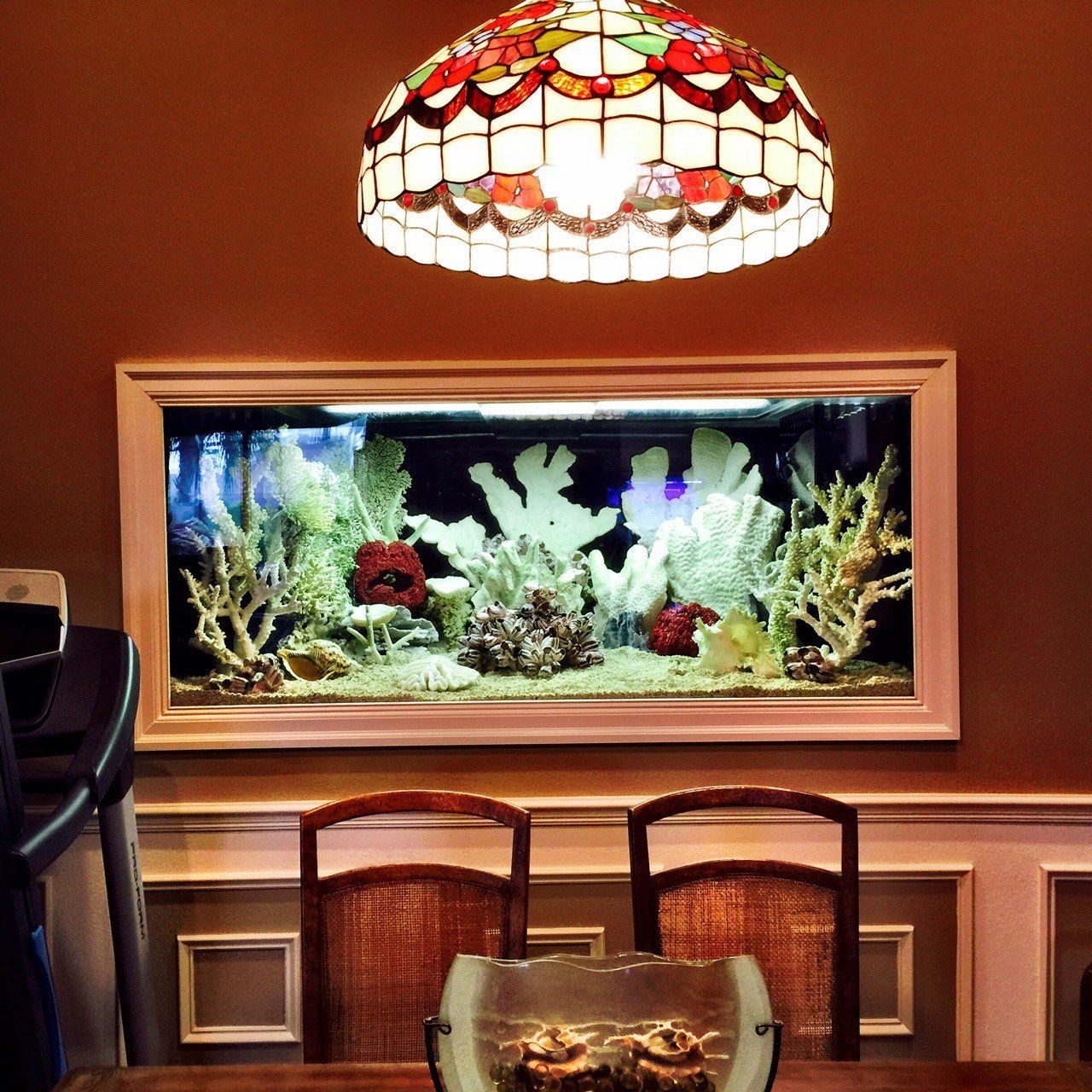 Dining room with aquarium built into the wall. Tiffany-style lamp overhead, two chairs at the table.
