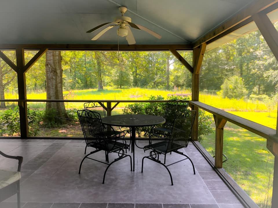 Screened-in porch with round table and chairs overlooking a green yard and trees.