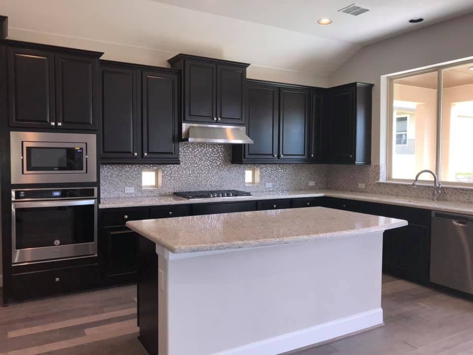 Dark kitchen cabinets with stainless steel appliances, white island and countertops.