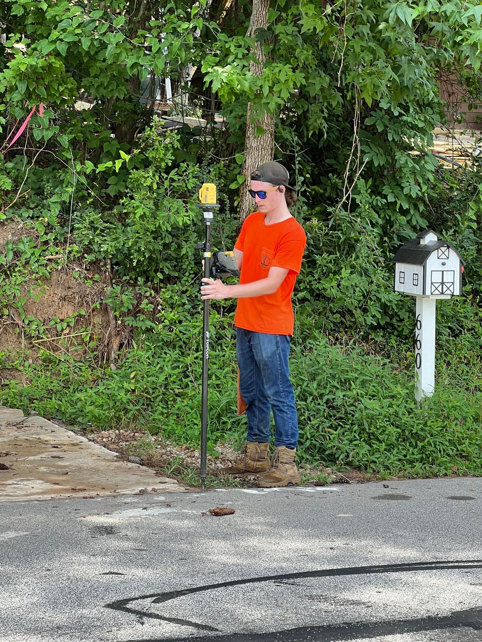 A man in an orange shirt is standing on the side of the road holding a pole.