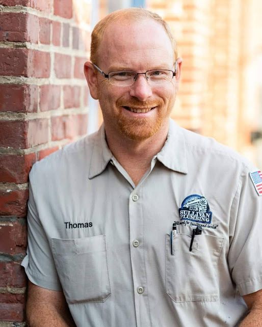 A man with a beard and glasses is leaning against a brick wall