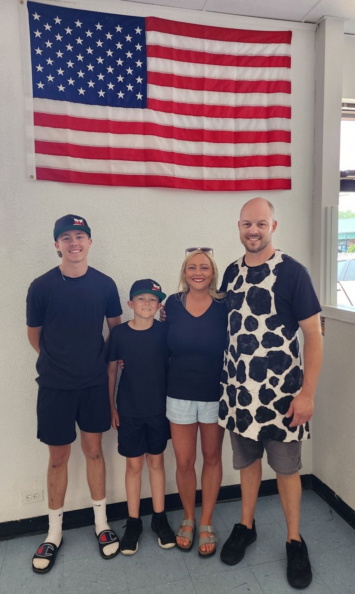 A family of four poses in front of an American flag. Two boys, a woman, and a man in a cow-print shirt smile.