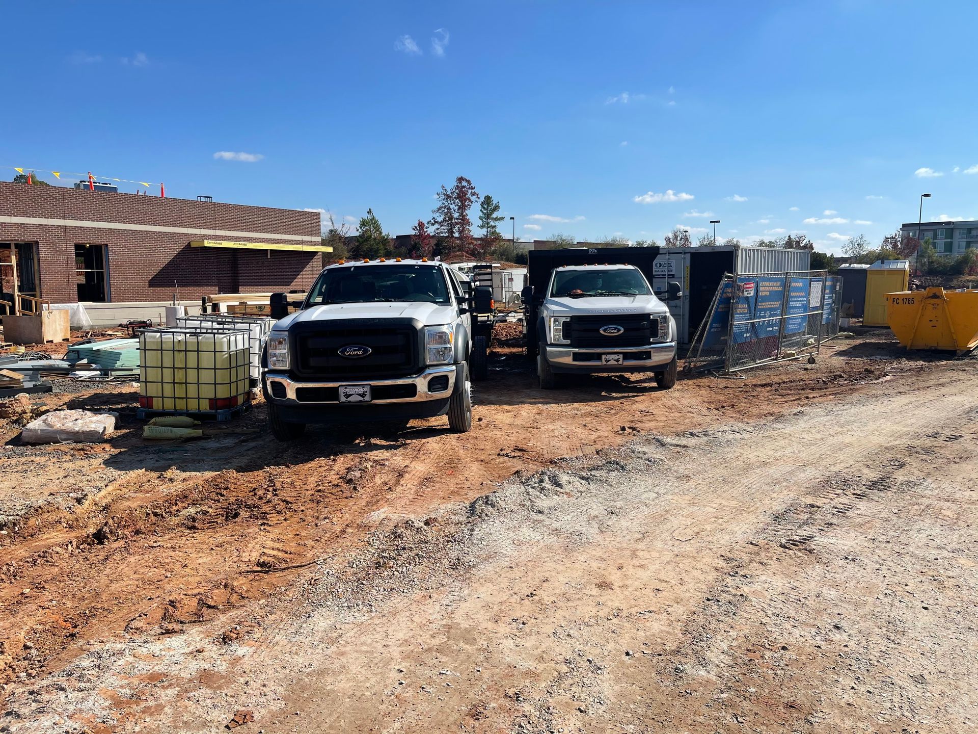 Two construction trucks are parked on the side of a dirt road.
