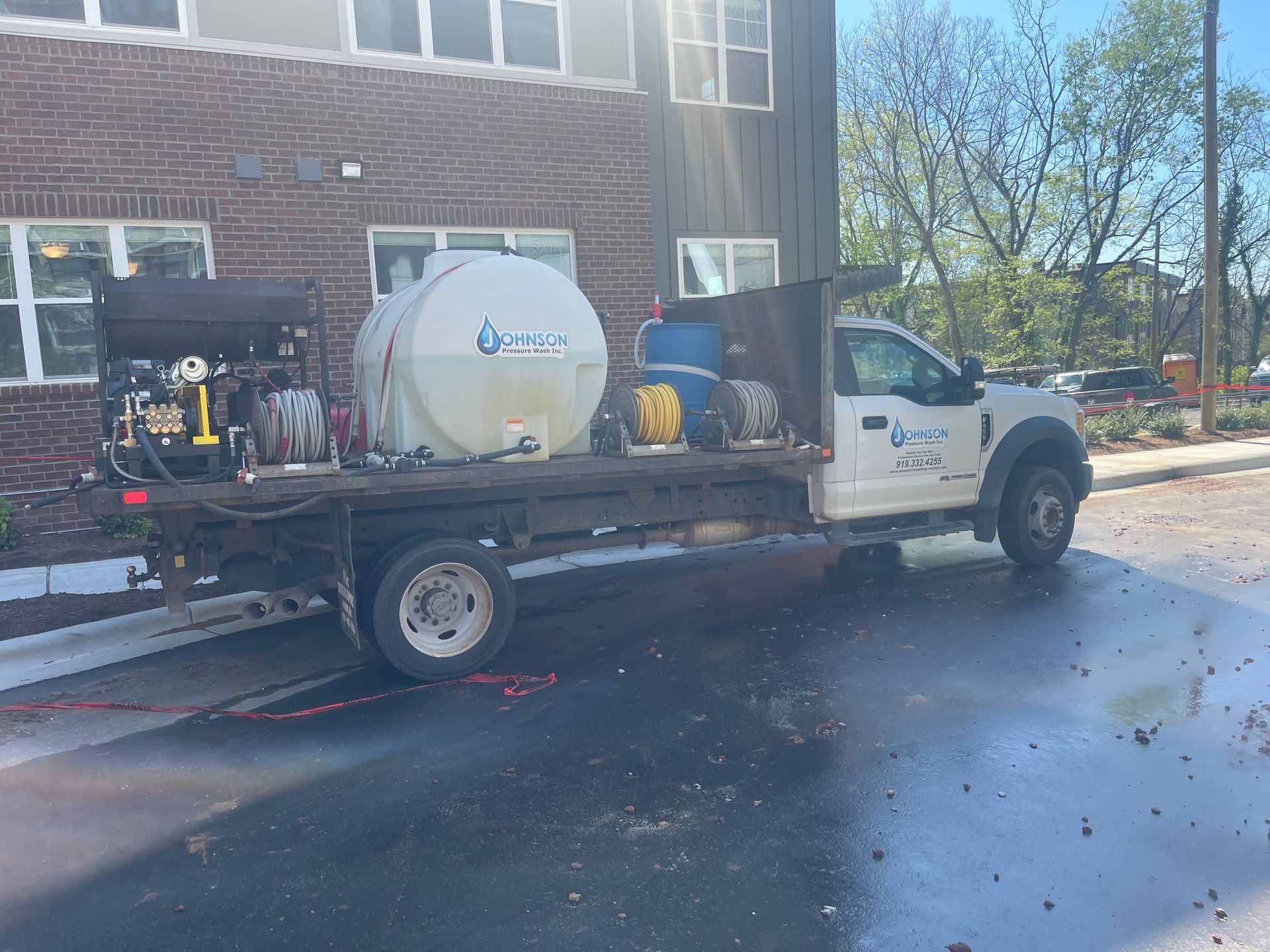 A white truck with a tank on the back is parked in front of a brick building.