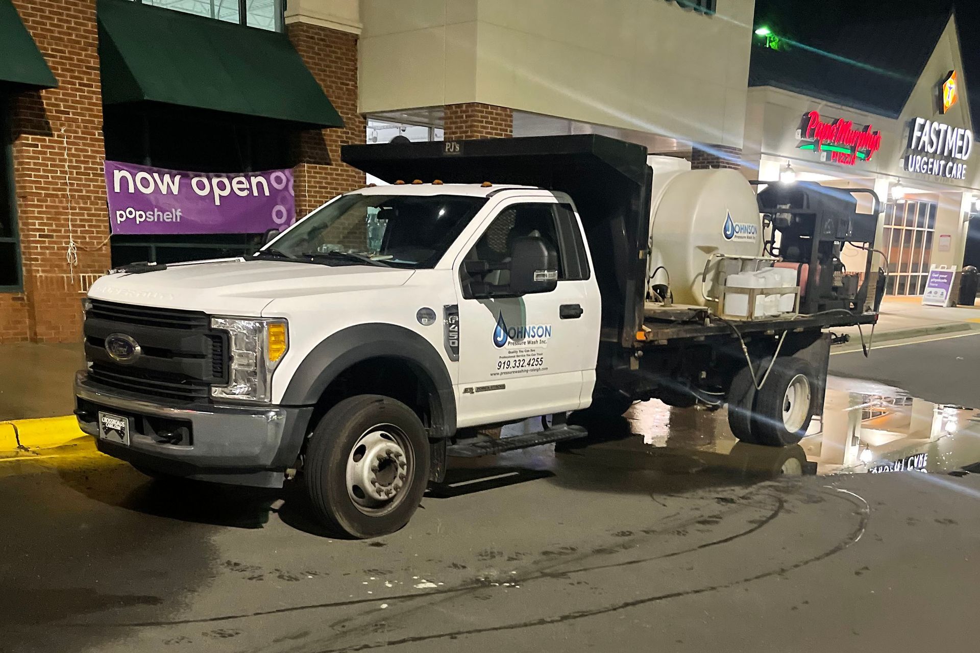 A white truck is parked on the side of the road in front of a store.