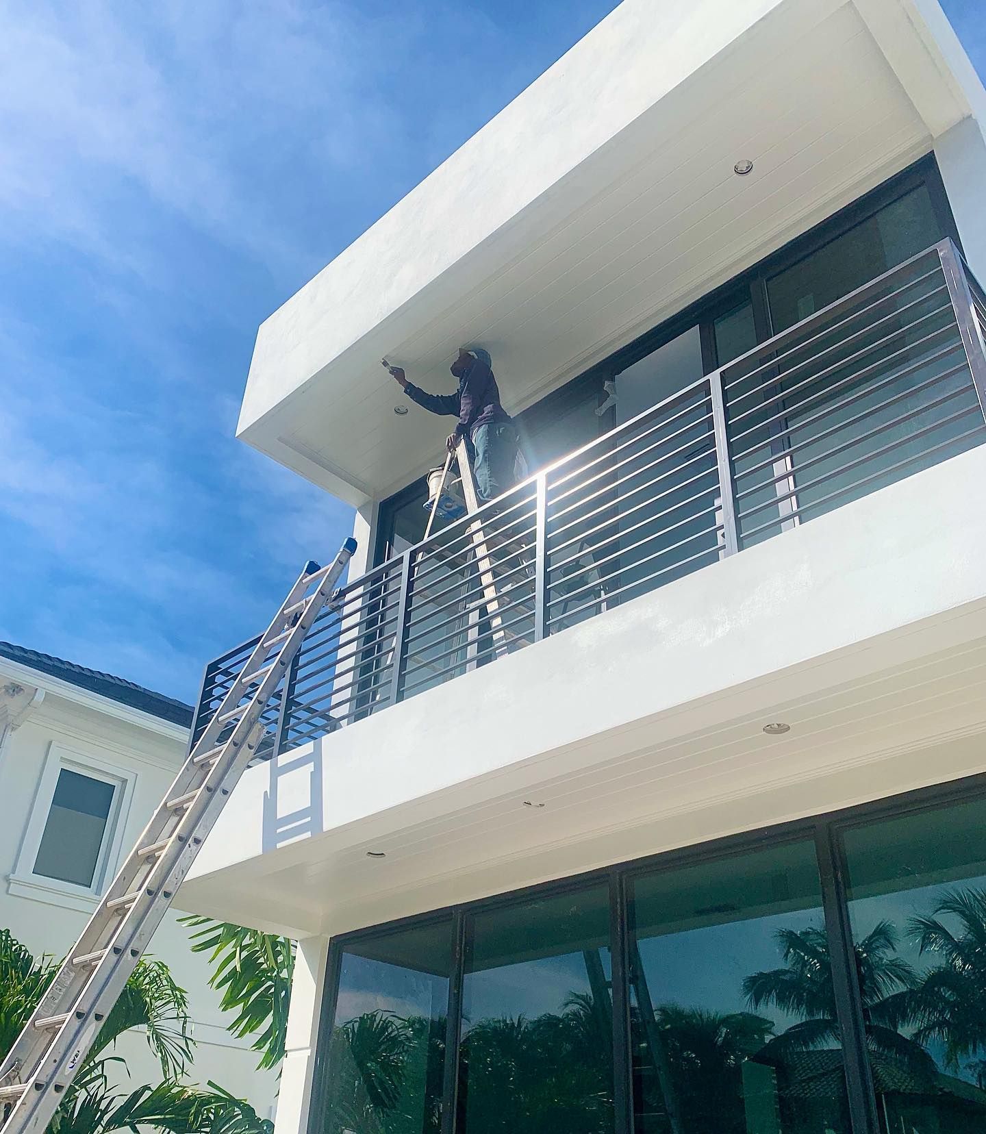 A man on a ladder is painting the garage door of a house