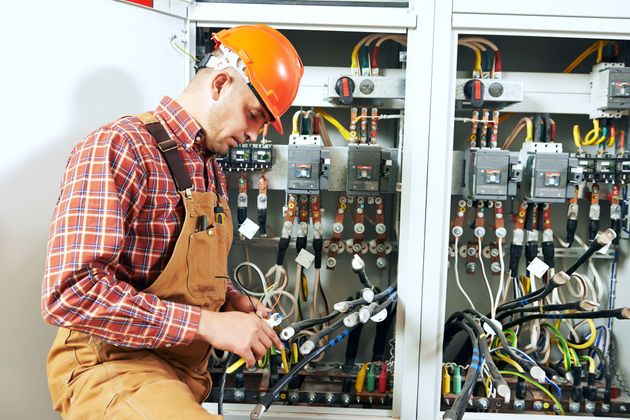 Electrician in orange hard hat working on electrical panel wiring.