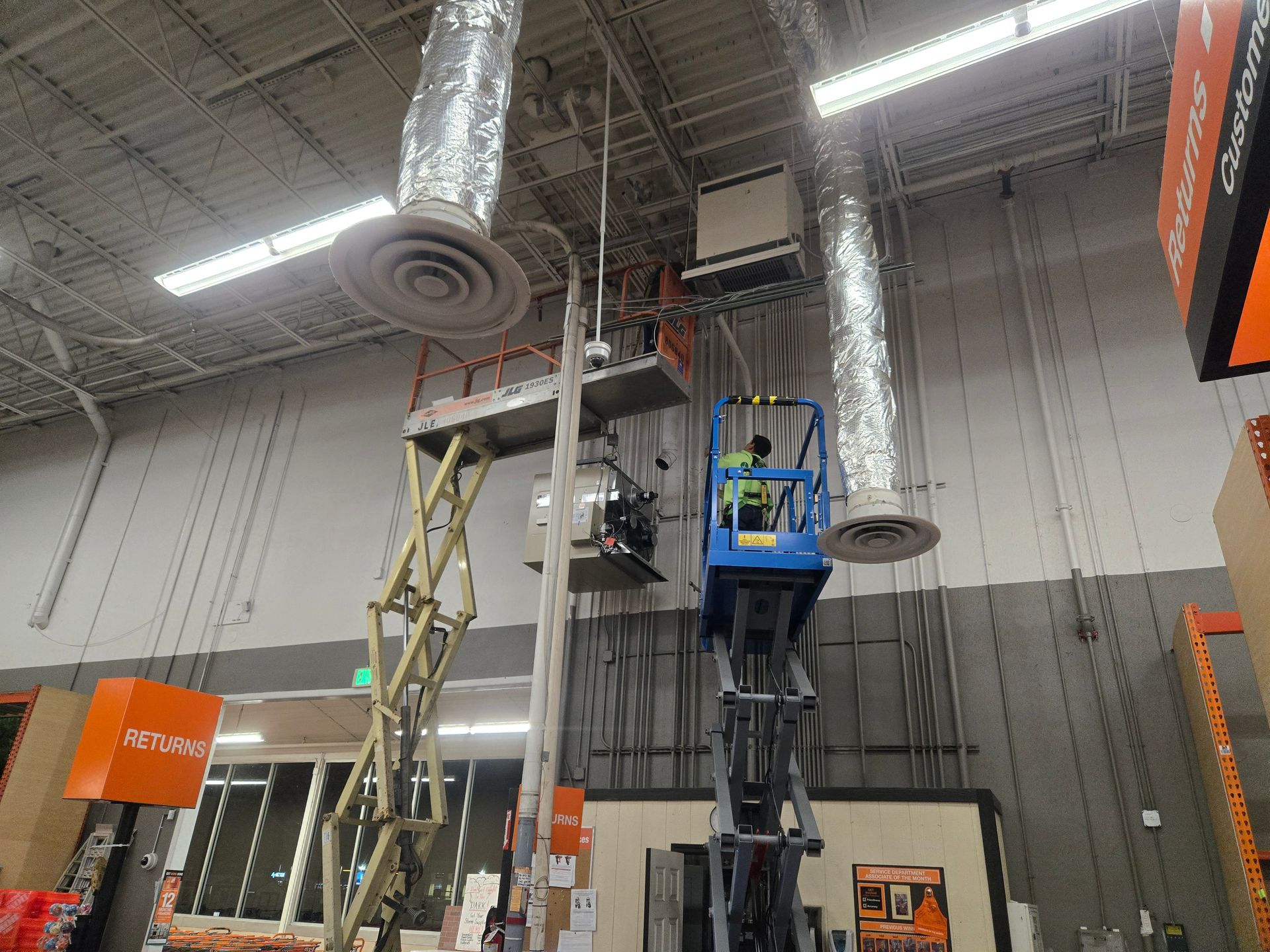 Workers on lifts installing or repairing HVAC ductwork inside a retail store.