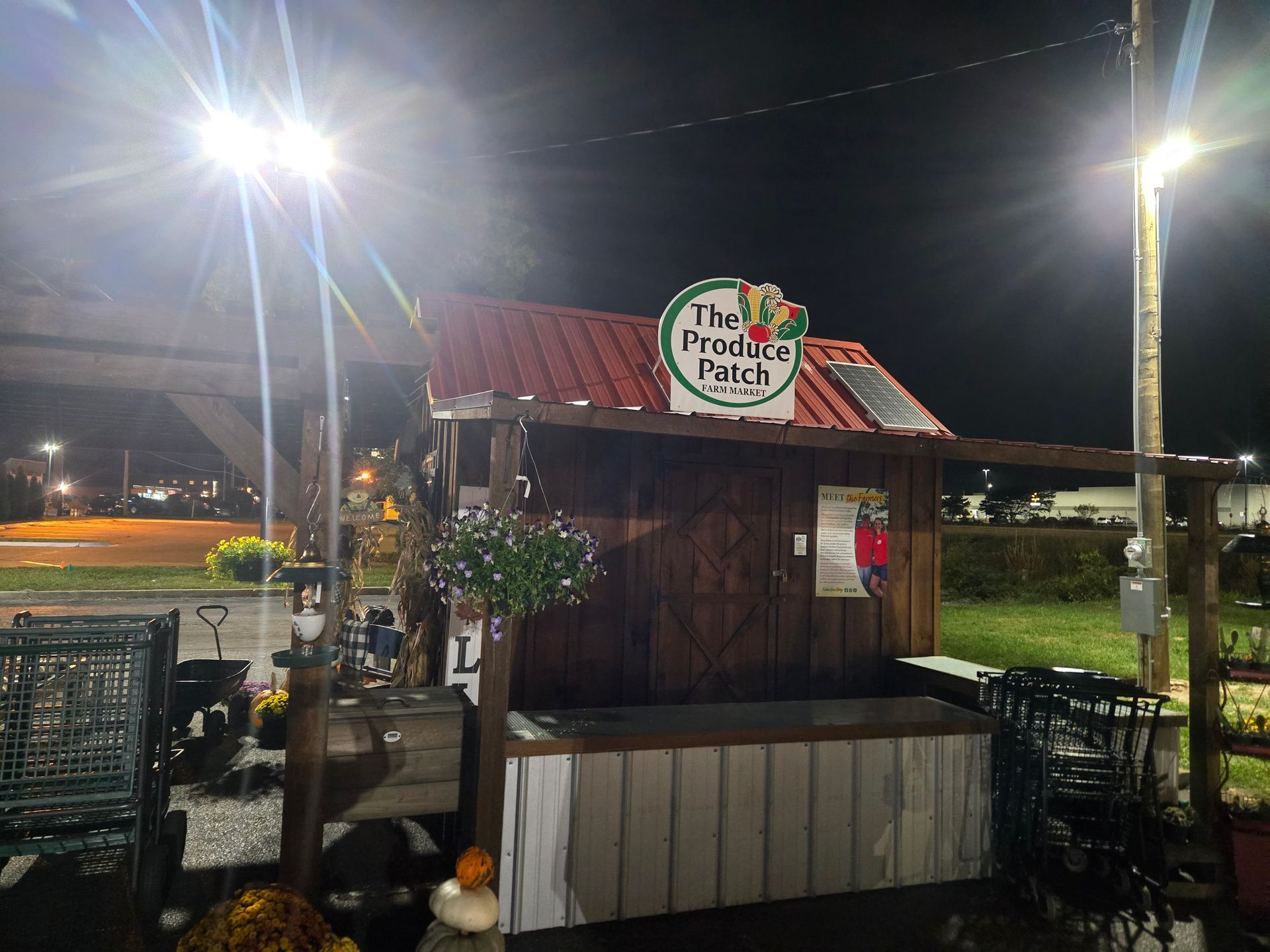 Produce stand at night under bright lights with a red roof and a sign that reads 