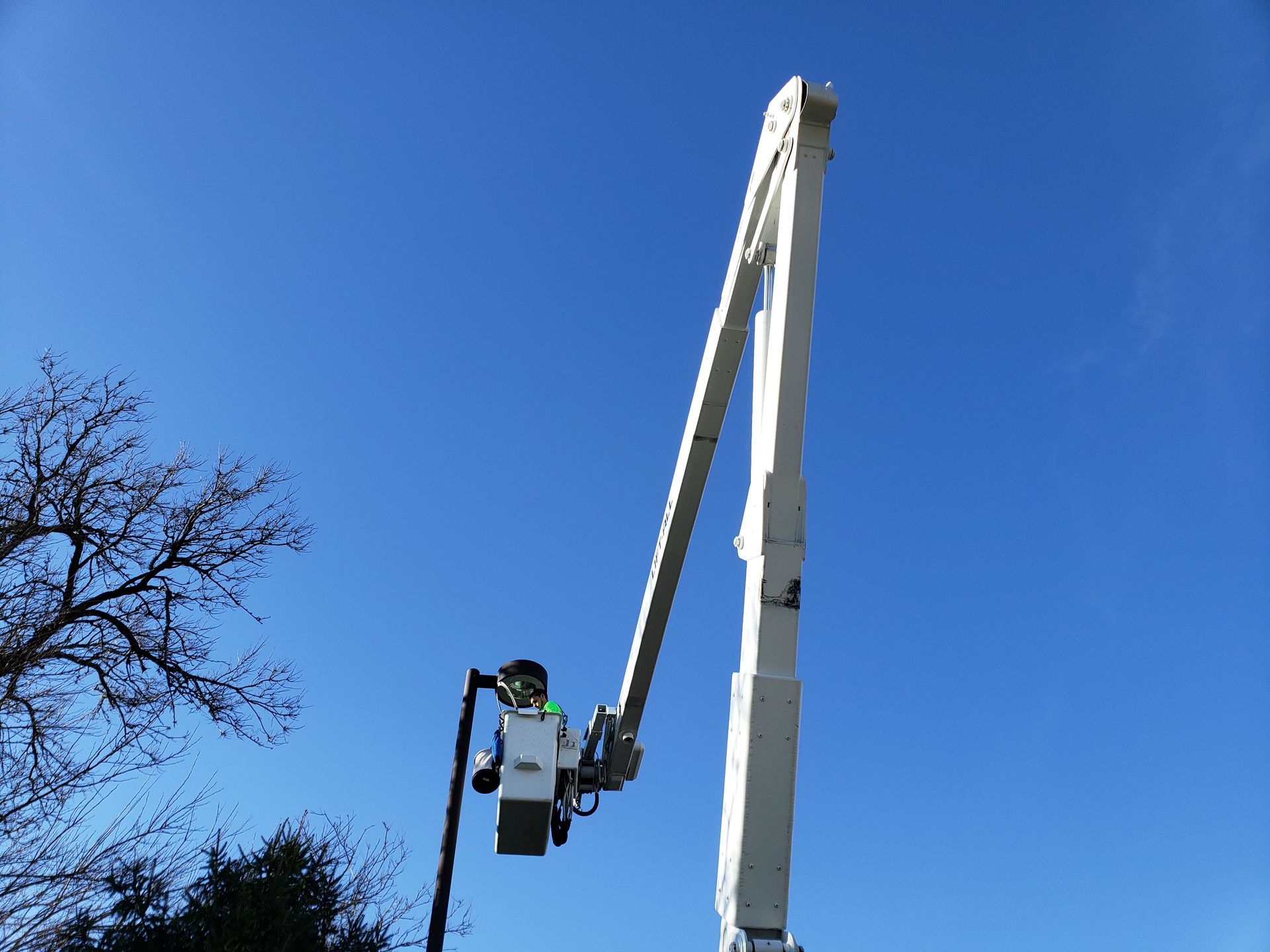 White boom lift with a worker bucket raised against a clear blue sky.