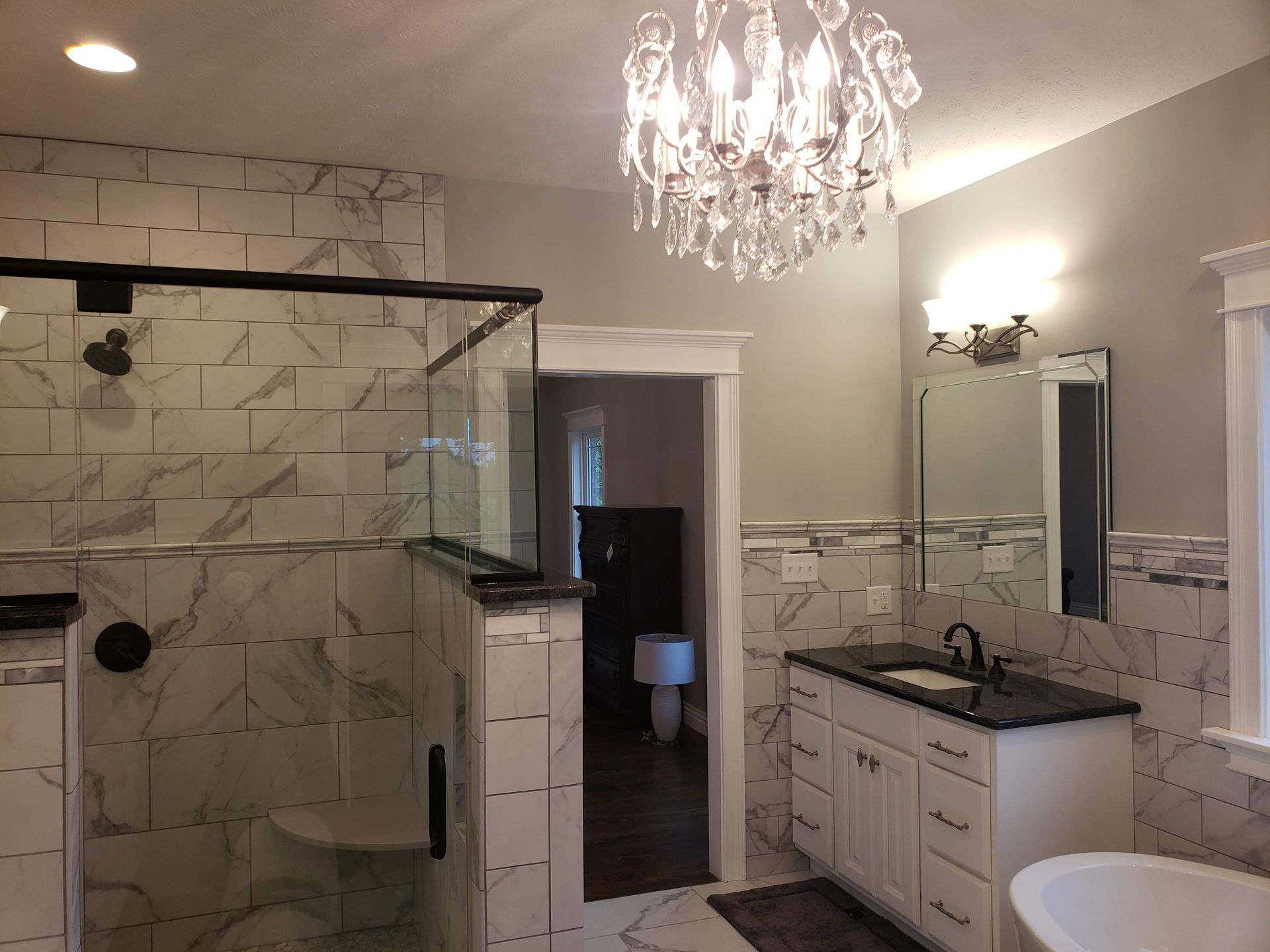 Bathroom with tiled shower, vanity, and chandelier; neutral colors.
